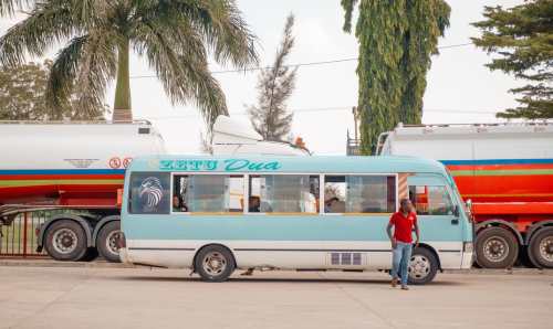 Man stood in front of a blue minibus and two oil tankers