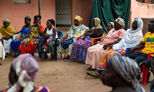 Women in a circle sat chatting outside in a village